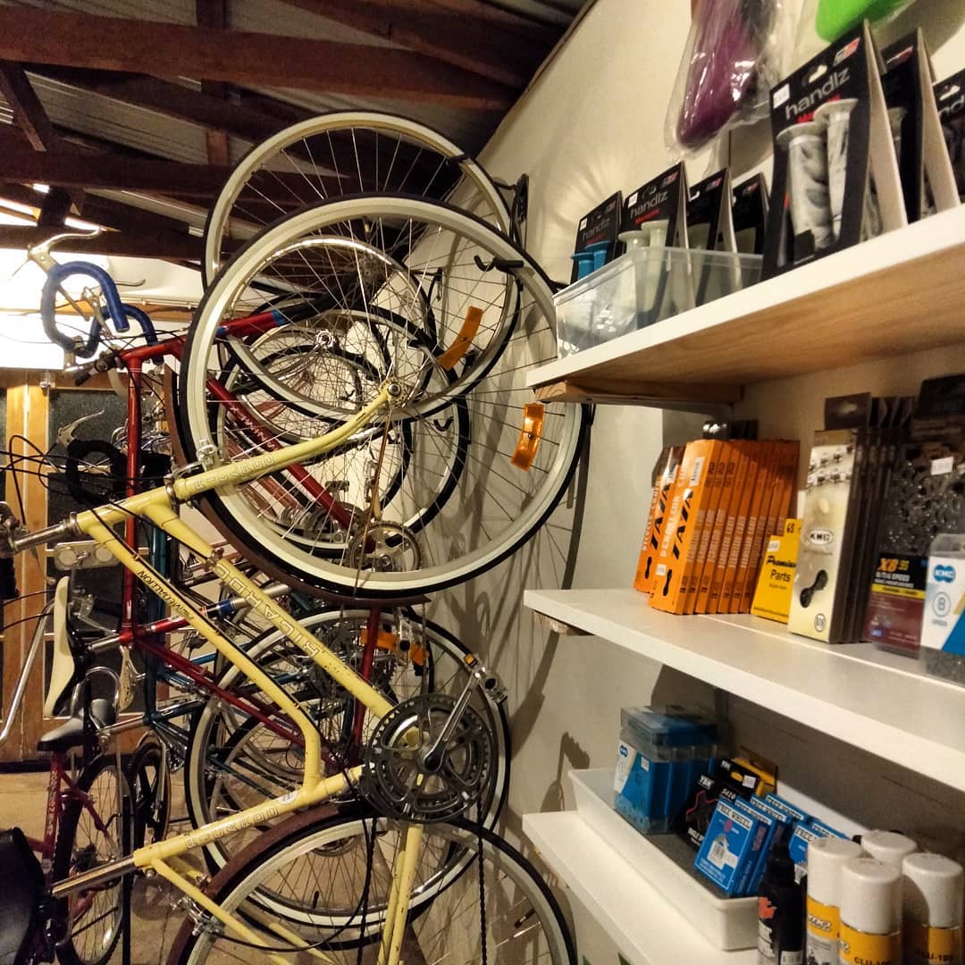 Vintage road bikes stacked against the workshop wall beside shelves of chains and tubes
